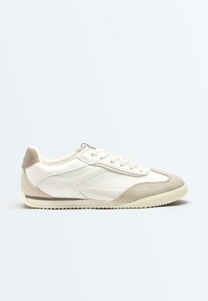 White low-top sneaker with light beige suede toe and heel accents, lace-up closure, and textured rubber sole.