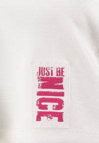 Camiseta blanca de algodón con un parche gráfico rectangular que lleva el texto "JUST BE NICE" en una fuente rosa fuerte y efecto ligeramente desgastado.