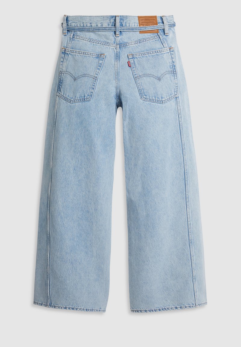 Jean large en denim bleu clair avec taille haute, comportant des poches arrière doubles et une étiquette en cuir sur la ceinture.