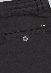 Black fabric shorts with back pocket, featuring a silver button and a small orange accent near the pocket's edge.
