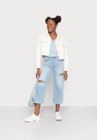 Lysvaskede ripped jeans, en cropped hvit denimjakke og en blå topp. Hun bærer en lyseblå veske og har på seg hvite sneakers.