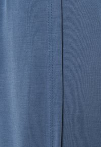 Tissu bleu avec une texture lisse, comportant un détail de couture sur le côté droit. Le matériau est léger et a un léger éclat.