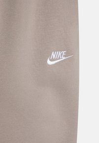 Nike világos bézs színű melegítőnadrág, sima textúrával, rugalmas derékrésszel és fehér hímzett logóval a bal combon.