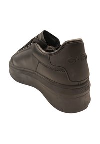 Sneaker nera in pelle con superficie testurizzata, suola in gomma spessa e forma arrotondata. Presenta un logo del marchio ben visibile sul tallone e sui lacci.