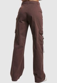 Bruna cargobyxor med lös passform, sidfickor och snörningsdetalj i midjan. Tillverkade av hållbart material med en mjuk yta.