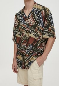 Camisa de manga corta, con cuello, que presenta un patrón abstracto multicolor en tonos tierra. Tejido ligero con un ajuste relajado.