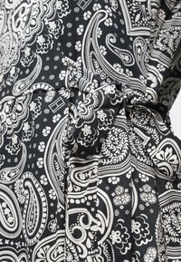 Čierno-biele látky s paisley vzorom, ktoré obsahujú zložitú kvetinovú výzdobu a textúrovaný povrch; má viazaný detail v oblasti pása.