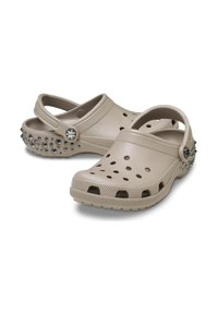 Beige Clogs mit Belüftungslöchern, strukturiertem Fußbett und einem strukturierten Riemen. Die Ferse hat dekorative silberne Nieten für zusätzlichen Detail.