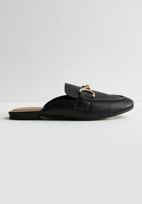 Černá kožená nazouvací bota zaoblenou špičkou a dekorativním zlatým kovovým prvkem na přední straně, s rovnou podrážkou a minimálním prošitím.