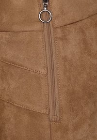 Brun faux-suede tyg har en centrerad silvermetalldragkedja med ett runt drag, förstärkt av subtil sömdetaljering.