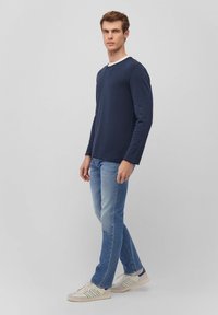 Navyblaues Langarm-T-Shirt mit geripptem Muster und weißem Rundhalsausschnitt, kombiniert mit hellblauen Jeans und weißen Sneakers mit grünen Akzenten.