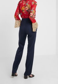 Blusa floral roja con mangas acampanadas largas de estampado de leopardo, combinada con pantalones de tiro alto en tonos marinos y sandalias de tacón negras. Ajuste suave y entallado.
