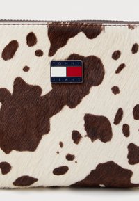 Prune ja valge laiguline lehmavaha rahakott, millel on metalli Tommy Jeans logo, sile tekstuur ja lukuga sulgemine.