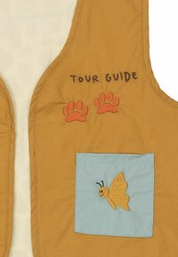 Chaleco de tela marrón etiquetado "GUÍA TURÍSTICO", con dos huellas de patas y un bolsillo azul con una mariposa bordada en amarillo.