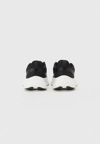 Mustat urheilukengät, joissa on teksturoitu verkkopäällinen ja valkoinen pehmustettu pohja, joka tarjoaa matalan designin ja vetolapun kantapäässä.