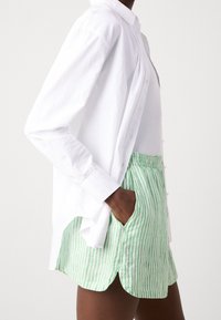 Biała koszula z guzikami i podwiniętymi rękawami w połączeniu z zielono-białymi spodniami w paski z bocznymi kieszeniami i luźnym krojem.