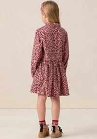 Robe à imprimé léopard rose avec une taille froncée, des manches longues et un col. Associée à un bandeau assorti et des chaussures beiges avec des accents noirs.