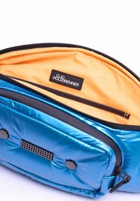 Blauwe gewatteerde rugzak met een oranje interieur, voorzien van een ritszak en een zwart etiket met "Clio Goldbrenner." Gladde, glanzende textuur.