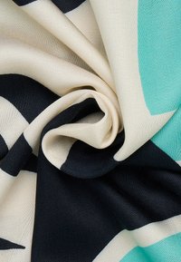 Mehrfarbiger Stoff mit einer weichen, glatten Textur; zeigt grüne und schwarze Formen auf beigem Hintergrund, die spiralförmig verdreht sind.