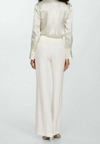 Kremowa jedwabna bluzka zestawiona z wysokim stanem kremowymi spodniami. Spodnie mają szerokie nogawki, gładką teksturę i elegancki, dopasowany krój.
