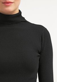 Svart ribbad polotröja med en åtsittande design. Tyget har en slät textur och ett enhetligt mönster av vertikala ribbor.