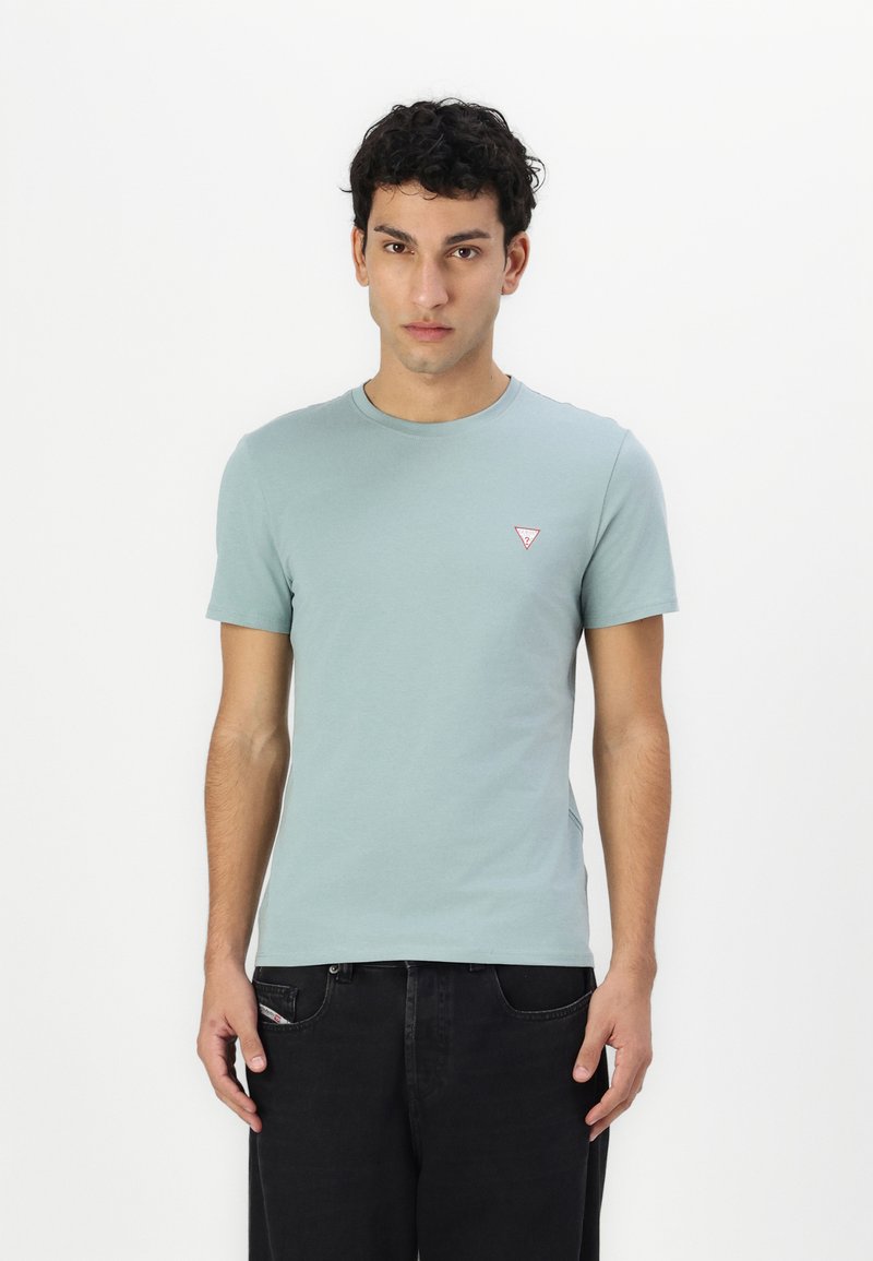Lys grøn bomulds t-shirt med korte ærmer, rund halsudskæring og et lille rødt trekantet logo på brystet. Bæres sammen med sorte jeans.