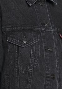 Svart denimjacka fram med knäppt ficklock, svarta metallknappar och synliga sömnadsdetaljer.