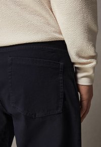 Navy blue cotton pants with a textured cream knit sweater. The pants feature a single back pocket with a straight seam design.