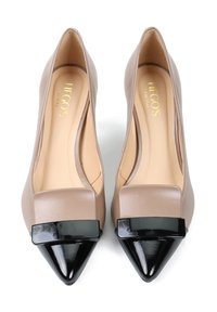 Para beżowych szpilek damskich z ostrymi noskami, z czarnymi połyskującymi czubkami i dużymi prostokątnymi czarnymi ozdobami na wierzchu.