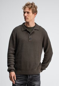 Dunkelolivgrüner, gerippter Strickpullover mit Kragen, Dreiknopfleiste und breiten Bündchen. Der Stoff wirkt weich und hat eine strukturierte Oberfläche.