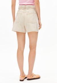Beige denim shorts with an elastic waistband, back pockets, and stitched detailing. Worn with orange strappy sandals.