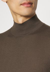 Pull en laine côtelé brun avec une coupe ajustée, un col montant et une texture lisse, idéal pour les superpositions.