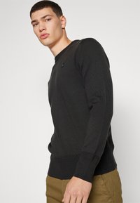 Dunkelgrauer langärmeliger Pullover mit gerippten Bündchen und Saum, rundem Ausschnitt und kleinem schwarzem Logo auf der Brust, aus einem strukturierten Stoff.