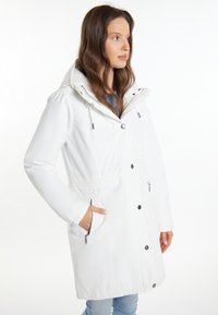 Hvid vandtæt parka med hætte, elastisk talje og flere lommer; har sort hardware og en glat tekstur.