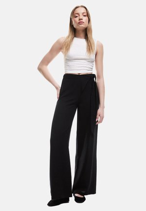 Witte cropped tanktop gecombineerd met zwarte high-waisted wijde broek, met een wikkeltie-accent rond de taille. Soepele, lichte stof.