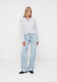 Hellgrauer, gestrickter Cardigan mit V-Ausschnitt, Knopfverschluss und geripptem Textil, kombiniert mit weit geschnittenen, hellblauen Jeans.