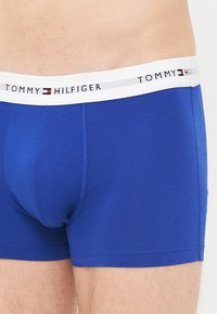 Blaue Baumwoll-Boxershorts mit einem weißen elastischen Bund. Der Bund ist mit schwarzem Markentext "TOMMY HILFIGER" und farbigen Logo-Akzenten versehen.
