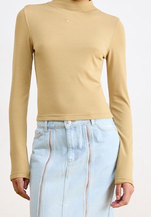 Haut beige à manches longues en maille côtelée avec petit logo Nike, associé à une jupe en denim bleu clair taille haute avec deux fermetures éclair verticales.