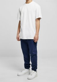 Bílé bavlněné tričko s krátkými rukávy, v kombinaci s tmavě modrými tepláky a bílými teniskami. Jednoduchý design, volný střih, bez viditelných vzorů.