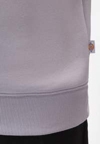 Grå sweatshirts med en mjuk textur, ribbat fåll och en liten märkesetikett på sidan. Enkelt, avslappnat design utan mönster.