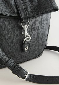 Zwarte rugzak van getextureerd leer met een klep, zilverkleurige hardware en een afneembare riem. Voorzien van een magnetische sluiting en gedetailleerd stiksel.