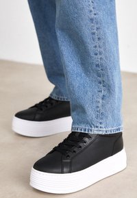 Czarne trampki na platformie z gładkiej skóry z białymi gumowymi podeszwami o żłobionej fakturze oraz sznurówkami zapewniającymi pewne dopasowanie.