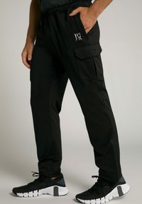 Zwarte sportbroeken met een elastische tailleband, zijzak met klep en logodetail. Gecombineerd met zwart-witte sneakers.