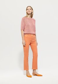 Pink textured knit sweater, orange flared jeans, orange flats with a low heel. Simple design and bright color palette.