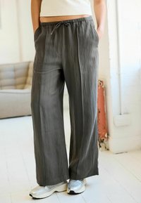 Pantaloni grigi a gamba larga realizzati in un tessuto leggero e liscio, con una cintura elastica e tasche. Indossati con sneakers argentate metallizzate.