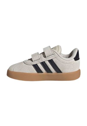 Zapatilla para niño pequeño de color beige claro con dos cierres de velcro, franjas negras de Adidas en el lateral y suela de goma marrón.