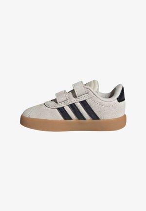 Scarpa da ginnastica beige chiaro per bambini piccoli con due cinturini in velcro, strisce Adidas nere sul lato e suola in gomma marrone.
