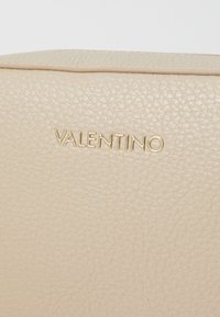 Sac à main en cuir beige avec finition texturée. Présente le logo en relief "VALENTINO" doré. Forme rectangulaire, détail de couture subtil.