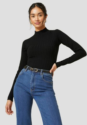 Mustmusturviga must turtleneck pikka varrukaga, kombineeritud kõrge vöökoht siniste teksadega ja must vöö, millel on kuldne sanga.