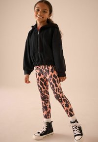 Haut zippé noir court avec une coupe décontractée, associé à des leggings à imprimé léopard rose et des baskets montantes noires avec des lacets blancs.